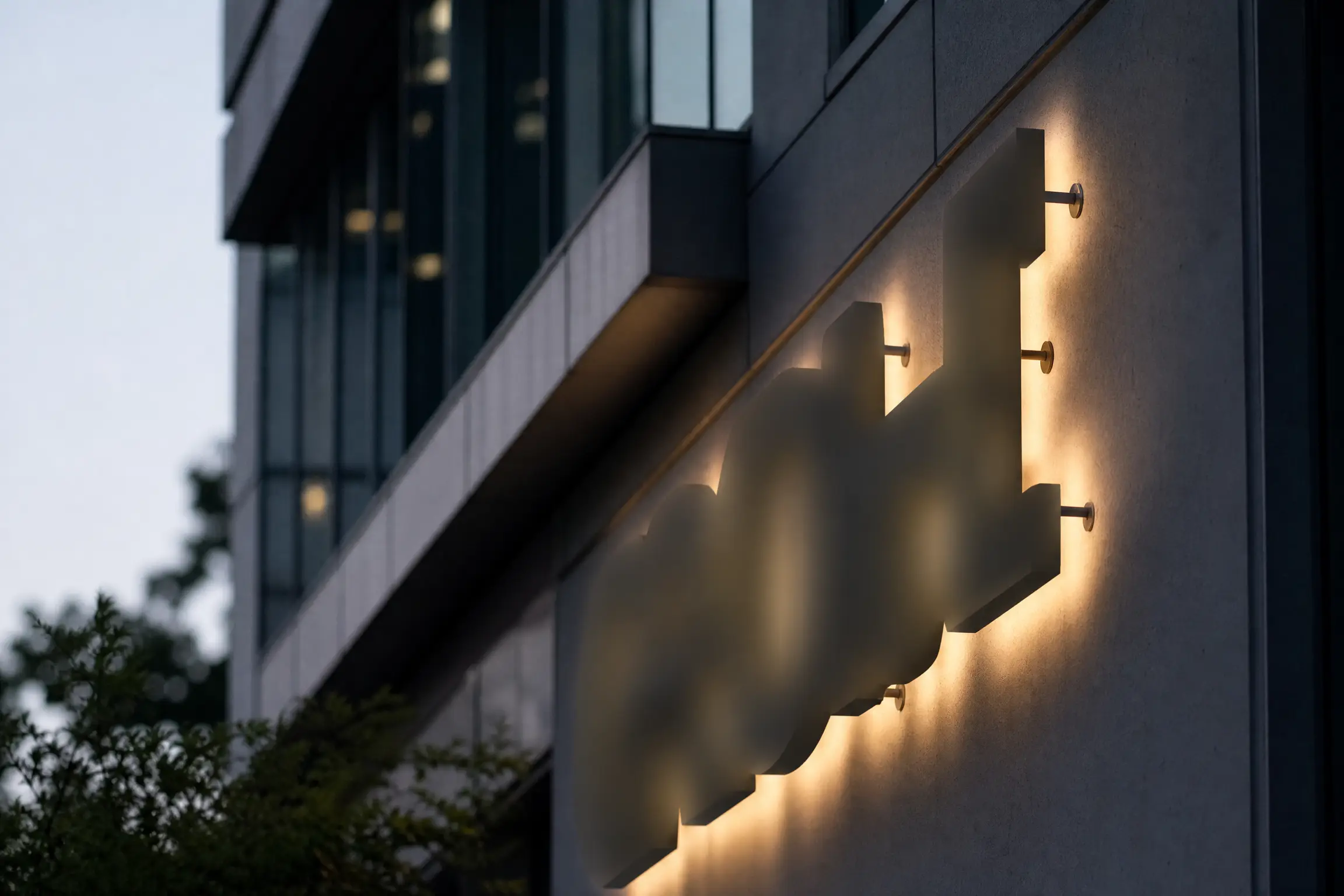 Façade d'immeuble de bureaux au crépuscule, lettres boîtier rétroéclairées créant un halo sur le mur
