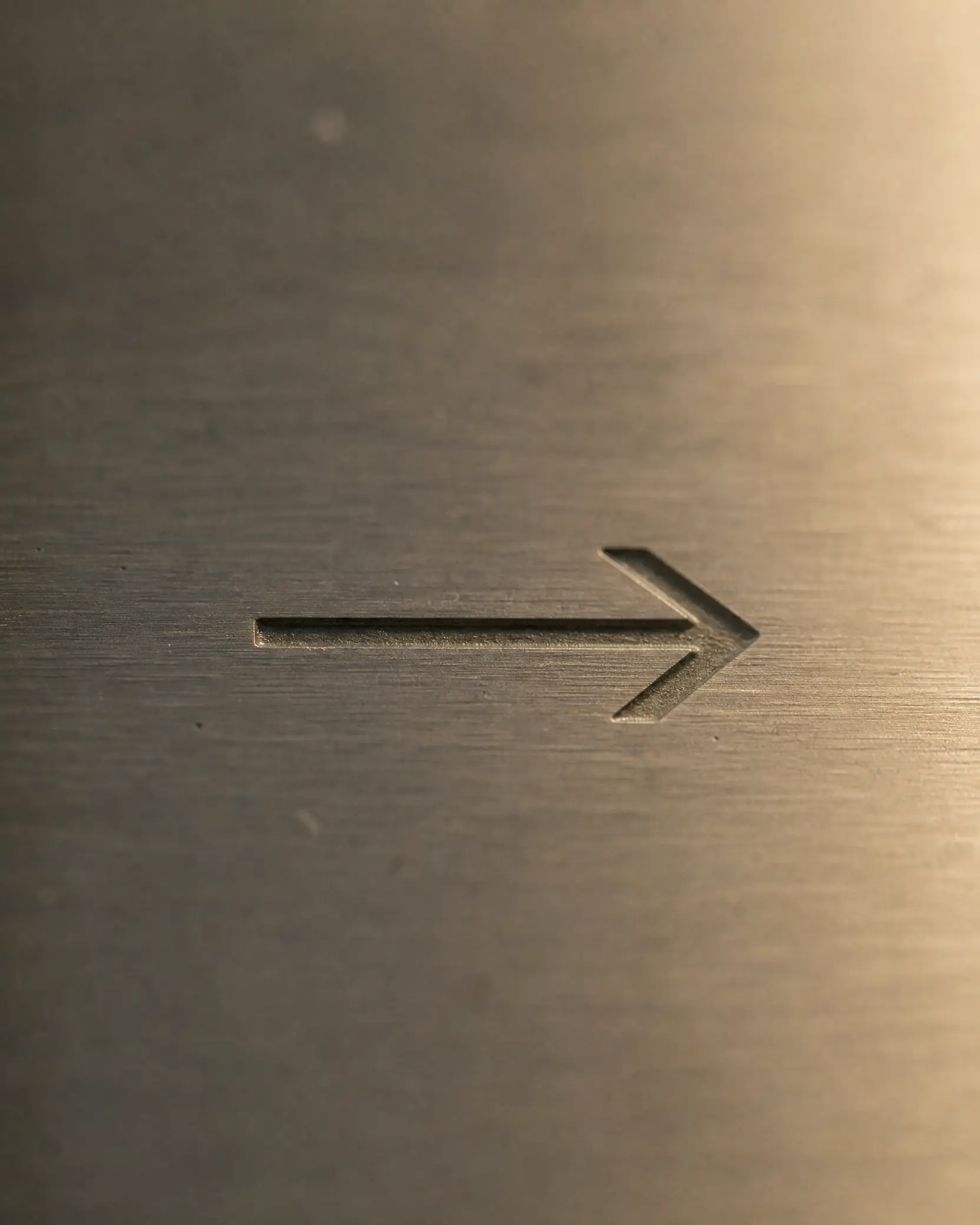 Directional arrow engraved on a brushed metal plate, raking light