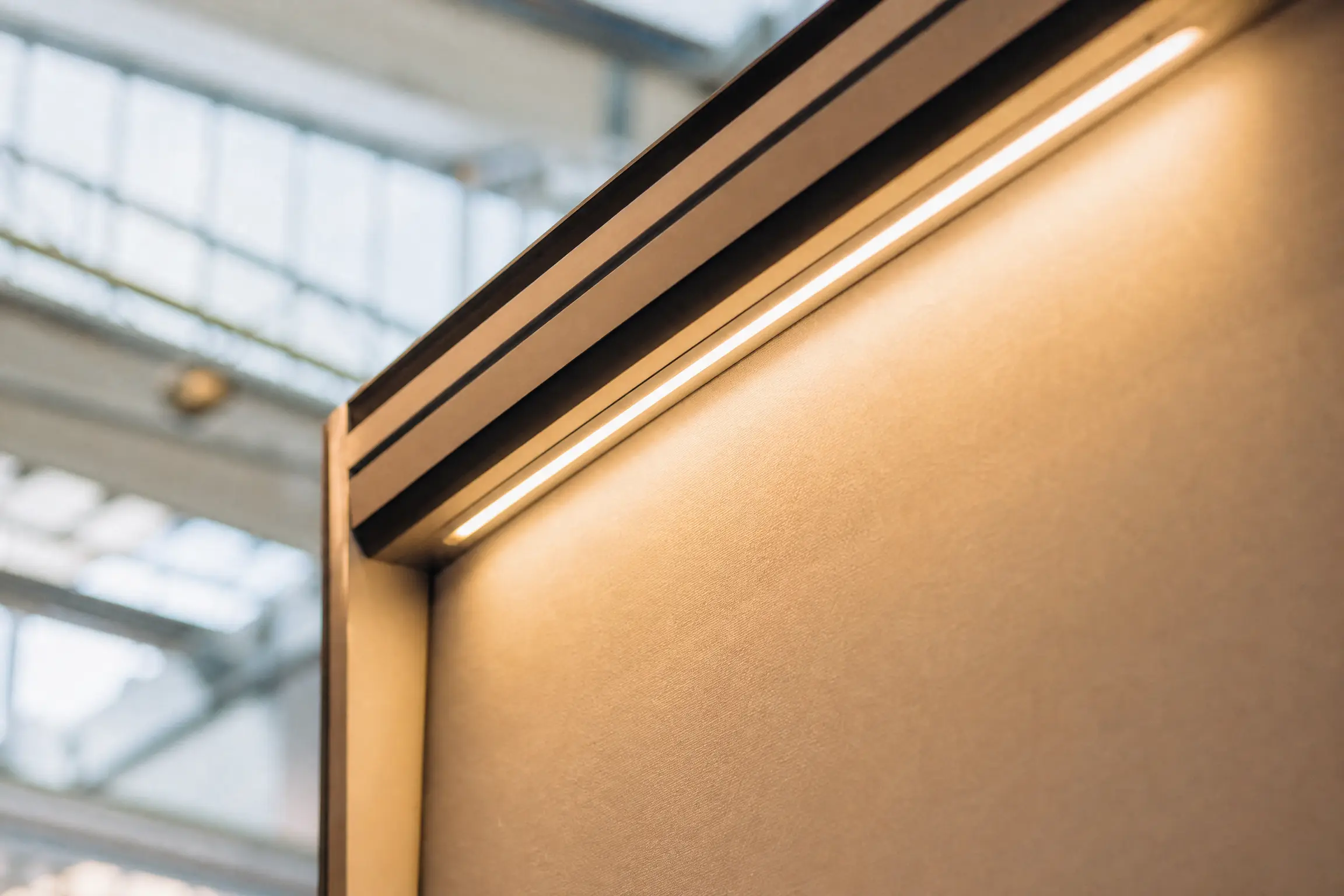 Regleta LED integrada en el friso superior de un stand, luz cálida cayendo sobre un panel textil tensado